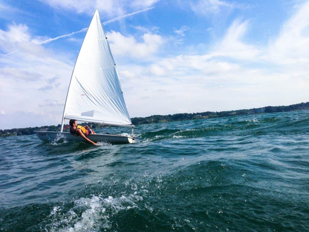 A one person dinghy sailing with a man leaning over the side with his hand in the water