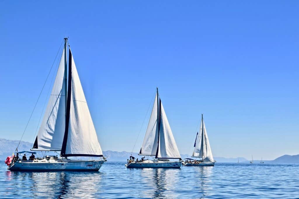 3 sail boats of different sizes sailing across calm water