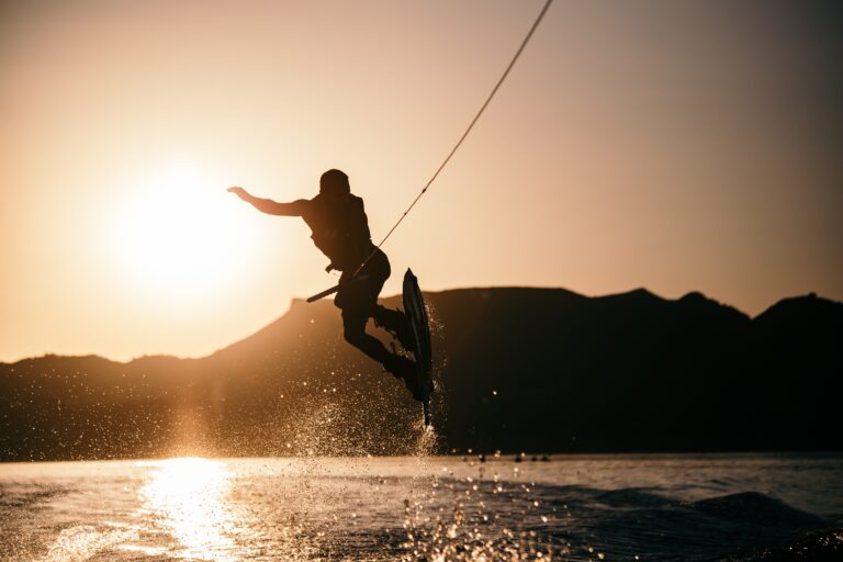 Wakeboarding with a sunset behind and the wakeboarder is jumping up in the air off the wake