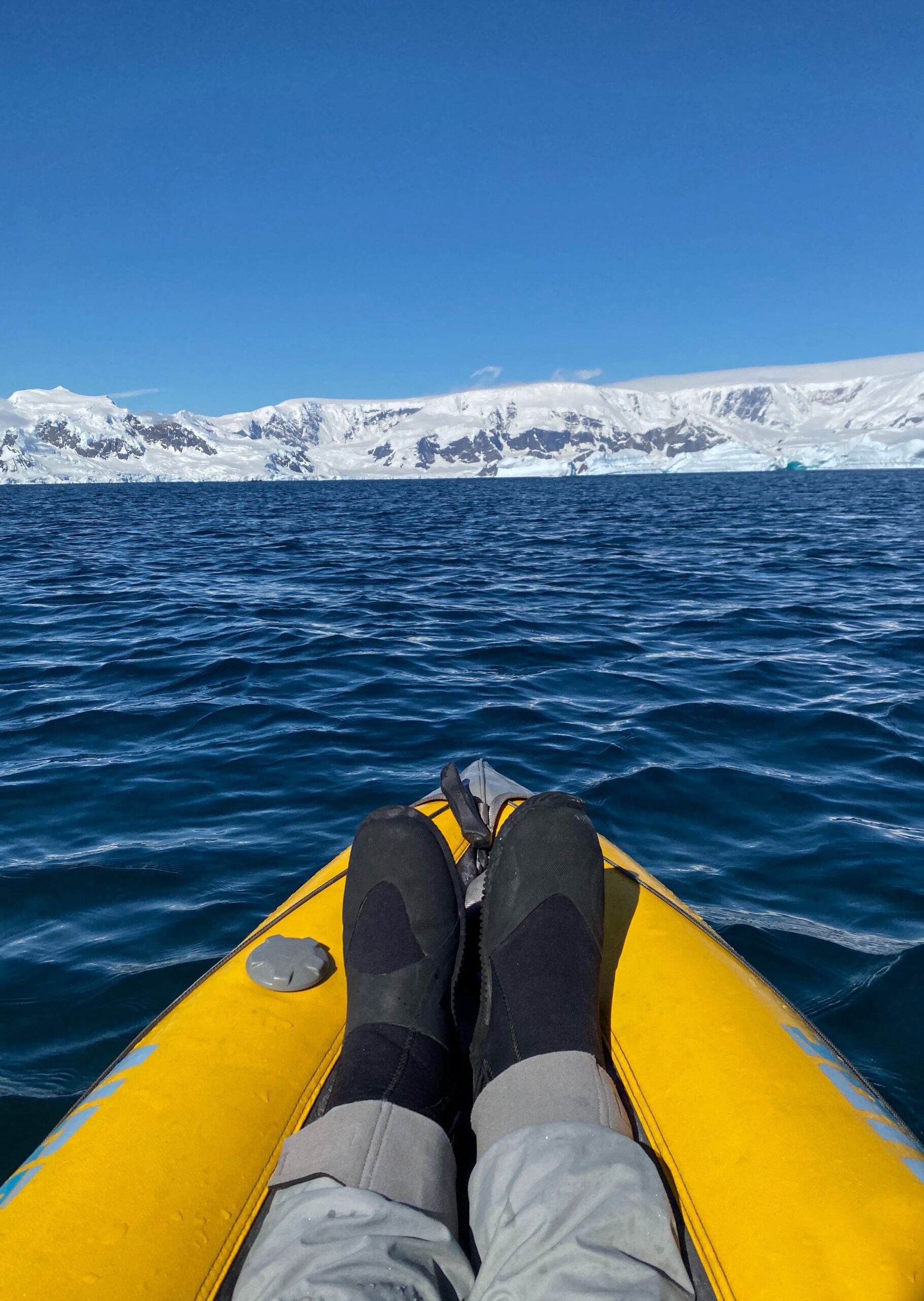 Persons feet in an Inflatable Kayak and an ice cliff in the distance