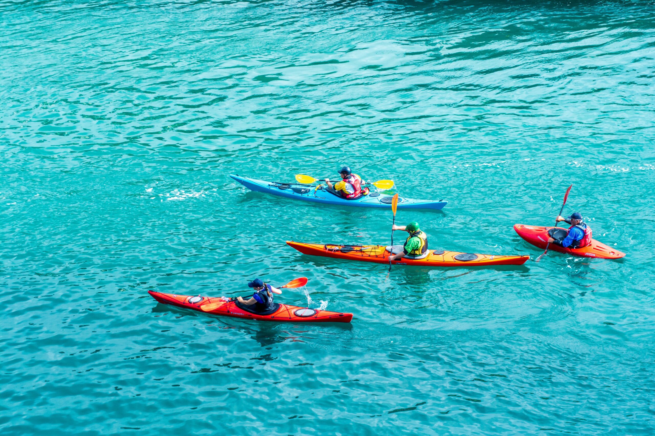 Kayaking for Beginners, four kayakers paddling across clear water